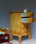 Belles and Whistles Distressed Damask - A1 Rice Decoupage Paper 
This is a beefy, mid-height dresser resting on a base with four beefy legs.  It is painted in Rebel Yellow CMP and is highly distressed.  The two top drawers are pulled out and the runners have been decoupaged.  There is lose, blue fabric draped behind the dresser.  To the left of the dresser, on the floor, is an old fashioned, red radio with flowers on top.