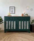 Belles and Whistles Enchanted Garden - Stencil provides an extra decorative touch to any project! Dark green painted dresser makeover with gold hinges. Enchanted Garden Stencil design applied in white on the door fronts. Staged with 2 stacked books with a short round glass vase with a candle inside. Orange terracotta pot, beige candlestick, and a beige pot containing a long vine of faux greenery.