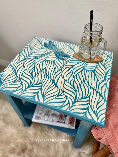 Belles and Whistles Enchanted Garden - Stencil provides an extra decorative touch to any project! Blue painted end table with the Enchanted Garden Stencil design applied on top with a dragonfly. Staged with a clear mason jar on a wooden coaster on top.