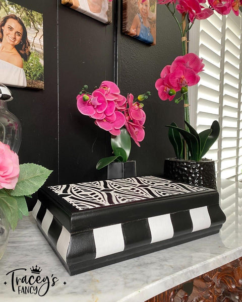 Belles and Whistles Geometric Moderne - Stencil provides an extra decorative touch to any project! Jewelry box painted in white and black with Geometric Moderne - Stencil used on top. Staged around piece is two pink orchid in blank planters Infront of black wall.