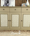 Belles and Whistles Greek Key - Stencil provides an extra decorative touch to any project! Tan colored vanity with Greek Key - Stencil on front of doors with bronze hardware. Staged on off-white carpet with brown wall, parrot statue with picture frame on right side and a picture frame of a koala on left side on top of dresser.