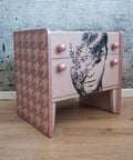 Belles and Whistles Houndstooth - Stencil provides an extra decorative touch to any project!
A light pink bedside dresser with the side panels covered in Houndstooth - Stencil with a lighter pink. Staged with laminated wood floor and a gray concrete looking wall.