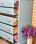 Belles and Whistles Houndstooth - Stencil provides an extra decorative touch to any project!
A chest of dresser with the drawers opened, the drawers are decorated with Houndstooth - Stencil. The opened drawers are showing the sides using the Floral Romance Transfer. Staged next to a ceramic vase with purple flowers inside.