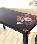 Belles and Whistles Roses - Silkscreen Stencil provides an extra decorative touch to any project! This image shows a black table with a flower transfer design on the right far side and also featuring our damask designed stencil in the corners on the top.