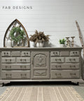 Large gray painted dresser staged in front of a white panel wall. The Royal Damask stencil has been applied in white on the front of some of the drawers.