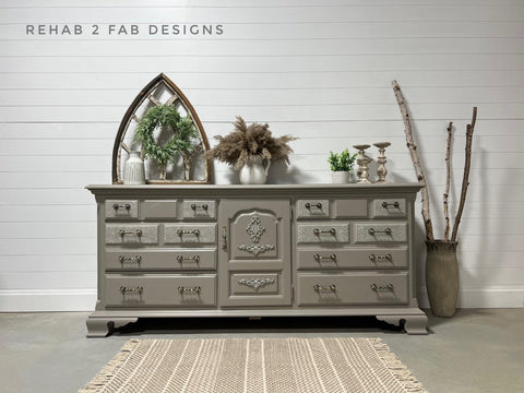 Large gray painted dresser staged in front of a white panel wall. The Royal Damask stencil has been applied in white on the front of some of the drawers.