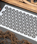 Belles and Whistles Trippy Blocks - Stencil provides an extra decorative touch to any project!  A picture of the Trippy Blocks stencil sitting on a black table with a brown net, brown flowers and a brown piece of wood around the stencil.