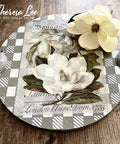Belles and Whistles Whimsical Check - Stencil provides an extra decorative touch to any project!  A round serving tray that has the Whimsical Check stencil chalk painted on it in silver and white.  The Magnolia Garden transfer is applied to the top center of the tray, and the tray handles are silver.  The tray sits on a brown wooden table with a magnolia sitting on the upper right side of the tray.