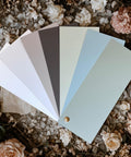A fan of six paint swatches in neutral and pastel shades arranged over a floral background with beige and blush pink flowers.