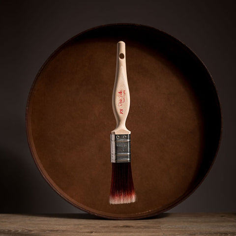 Paint brush with wooden handle and red bristle head floating in front of a dark brown circular platform.