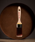 Paint brush with wooden handle and red bristle head floating in front of a dark brown circular platform.