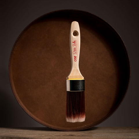 Paint brush with wooden handle and red bristle head floating in front of a dark brown circular platform.