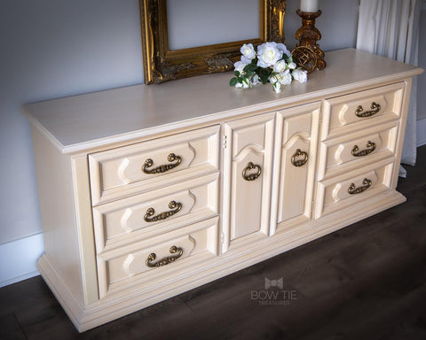 Dixie Belle Paint Apricot Chalk Mineral Paint is the perfect paint for any DIY project!
Dresser painted in Apricot Chalk Mineral Paint with bronze hardware, staged on top of the piece are white flowers, gold frame and a gold candle holder.