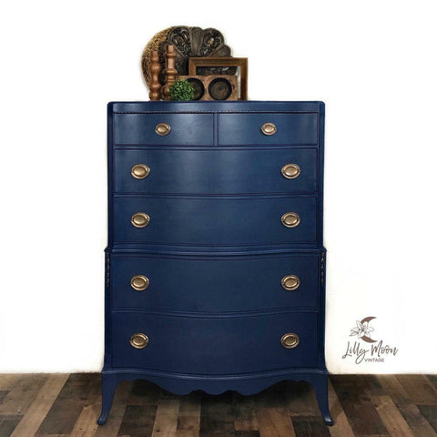 Dixie Belle Paint Bunker Hill Blue Chalk Mineral Paint is the perfect paint for any DIY project!
Chest of drawer painted in Bunker Hill Blue Chalk Mineral Paint with gold hardware and brown wooden decor on top of the piece. Staged in front of a white wall and brown wooden floors.