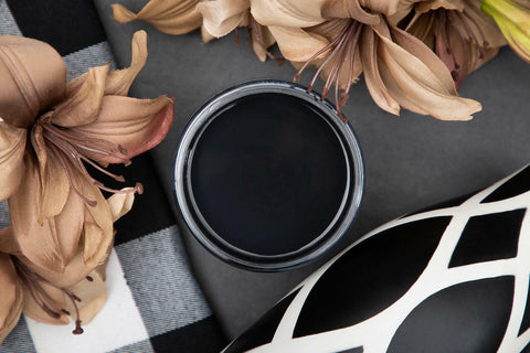 Dixie Belle Paint Caviar Chalk Mineral Paint is the perfect paint for any DIY project!
Top view of an opened container of Caviar Chalk Mineral Paint staged with tan flower, white and black checkered cloth on top of a black background.