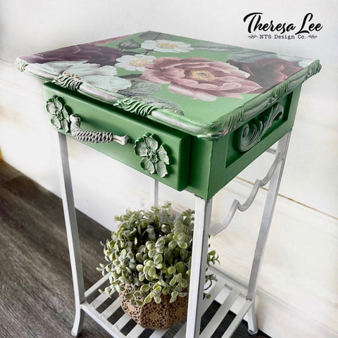 Dixie Belle Paint Chameleon Wax gives your furniture DIY project an iridescent glow and is sheer wax utilized to unveil the  highlight of your project!
Bedside table painted in green and white legs with Chameleon Wax along the edge and applique . As well as the Floral Romance Transfer on the top of table. Staged with a potted faux succulent under the table.