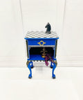 Dixie Belle Paint Cobalt Blue Chalk Mineral Paint is the perfect paint for any DIY project!
There is an ornate side table painted in cobalt blue CMP with gold painted wood -U-bend trim and knob.  There's a white and gray painted chess board painted on the top of the table with a large, black horse placed on the chess board and a Fleur de lis on the bottom shelf of the table and purple flowers hanging off the bottom shelf.l