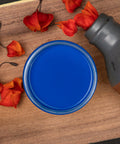 Dixie Belle Paint Cobalt Blue Chalk Mineral Paint is the perfect paint for any DIY project! An open jar of Cobalt Blue Chalk Mineral Paint is placed on a piece of No Pain Gel Stain with orange flowers placed around it and an old rusty canteen placed on it's side.
