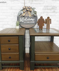 Two wooden side tables with a 'Welcome to our home' sign on a white brick wall background.