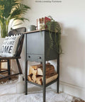 Dark green wooden sideboard with firewood, chair, and decorative items in a room setting.