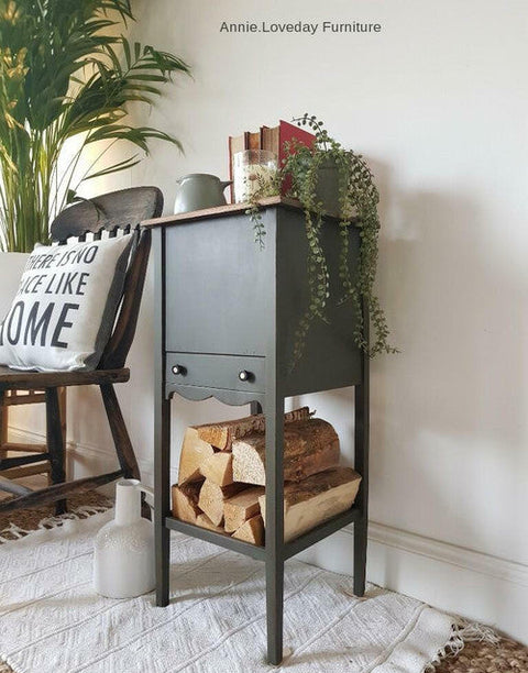 Dark green wooden sideboard with firewood, chair, and decorative items in a room setting.