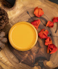 Dixie Belle Paint Colonel Mustard Chalk Mineral Paint is the perfect paint for any DIY project!
You are looking down on a can of Colonel Mustard so you can only see the paint inside.  The paint can is sitting on top of a large wood log.  On top of the log, next to the Colonel Mustard CMP are two pine cones to the left and to the right are orange flower pedals,  two has fallen to to the dark, wood floor.