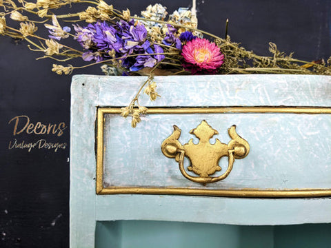 Dixie Belle Paint Dixie Dirt-4oz. 
Corner of dresser Painted blue marble with gold hardware and gold panel around drawer with Dixie Dirt around paneling. Staged on top of dress is a bundle of dried wildflowers.