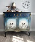 Dixie Belle Paint Dried Sage Chalk Mineral Paint is the perfect paint for any DIY project!
A beautiful buffet with a reverse ombre effect with a blend of blues on top fading down to Dried Sage Chalk Mineral Paint in the center door panels they're white with Bud & Branches - Transfer. Staged with bronze antique items on top with a white wall background.
