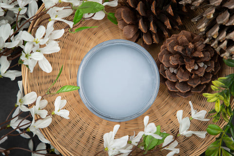 Dixie Belle Paint Dusty Blue Chalk Mineral Paint is the perfect paint for any DIY project! Open jar of Dusty Blue Chalk Mineral Paint staged in a woven basket with white flowers, greenery, and pine cones.