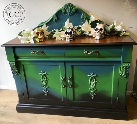 Dixie Belle Paint Evergreen Chalk Mineral Paint is the perfect paint for any DIY project! Green, blue, and black painted buffet with a medium stained top. Styled with faux white lilies on top along with 3 skulls, one is gold, one is black and white checkered, and one is silver.