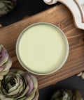 Dixie Belle Paint Farmhouse Green Chalk Mineral Paint is the perfect paint for any DIY project!
A look from directly above the paint looking into the paint can.  The paint can is siting on a stained, 2x6 board.  There are two flowers next to the paint can and a white tray on the other side of the paint.  The board is lifted off the ground.  Under the board is a string of wooden balls and two more flowers.
Opened container of Farmhouse Green Chalk Mineral Paint staged with mute green and purple roses on top 