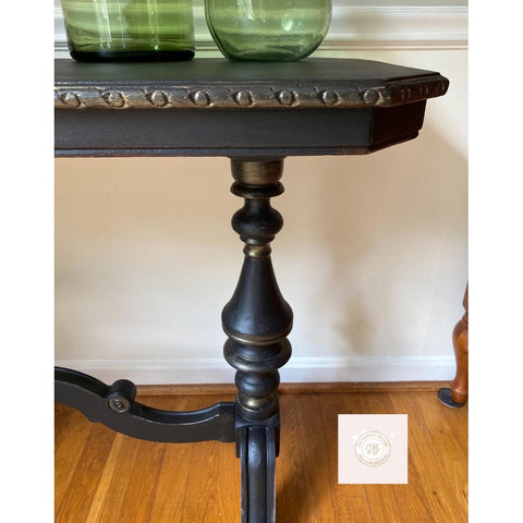 Dixie Belle Paint Gold Shimmer Glaze. Blacks table Leg using Gold Shimmer Glaze in high points and in crevasses to make the the piece have more dimension. Staged  on wooden floor with white wall.