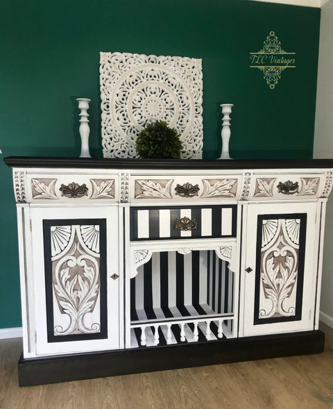 Dixie Belle Paint Grunge Glaze 
Beautiful fireplace white and black credenza with the Grunge Glaze inside the wood applique. Staged with white candle pedestaled and greenery on top of piece. on a green wall background.