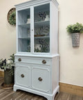 Dixie Belle Paint Haint Blue Chalk Mineral Paint is the perfect paint for any DIY project!
A kitchen hutch painted in Blue Chalk Mineral Paint with silver hardware. Stage with pitchers and teapots inside the hutch, As well as greenery around the piece.