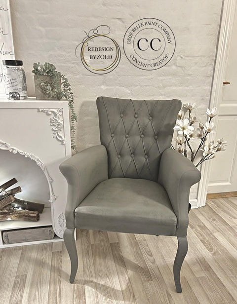 Dixie Belle Paint Hurricane Gray Chalk Mineral Paint is the perfect paint for any DIY project!
A Fabric cushion chair painted in Hurricane Gray Chalk Mineral Paint  staged next to a white fireplace in front of a white brick wall on top of a wooden floor.