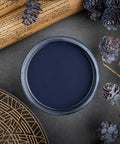Dixie Belle Paint In the Navy Chalk Mineral Paint is the perfect paint for any DIY project!
A top view of an opened container of In the Navy Chalk Mineral Paint, staged with pinecones painted with In the Navy CMP along with scrolls and a black and old plate.