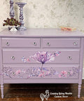 Dixie Belle Paint Lucky Lavender Chalk Mineral Paint is the perfect paint for any DIY project!
Dresser painted in Lucky Lavender CMP with Translucent Garden - Transfer across the the long drawers with crystal hardware. Staged on wooden floor and two lavender distressed candle holders on top.