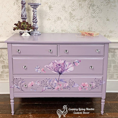 Dixie Belle Paint Lucky Lavender Chalk Mineral Paint is the perfect paint for any DIY project!
Dresser painted in Lucky Lavender CMP with Translucent Garden - Transfer across the the long drawers with crystal hardware. Staged on wooden floor and two lavender distressed candle holders on top.