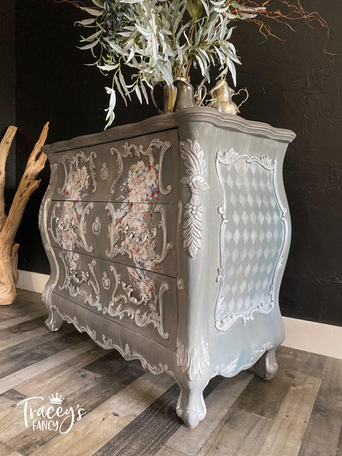 Dixie Belle Paint Mason Dixon Gray Chalk Mineral Paint is the perfect paint for any DIY project! Chalk Painted gray Side table with Stencil squares on the side and florals on the front of drawers, with white painted accents all around it. Staged with some plants on top.