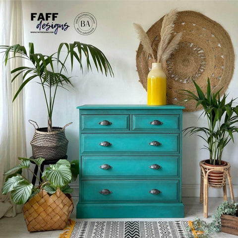 Dixie Belle Paint Mermaid Tail Chalk Mineral Paint is the perfect paint for any DIY project! Teal Chalk Painted Dresser staged with some potted palm trees, a yellow vase with wheat in it and a boho style rug and wall hanging décor.