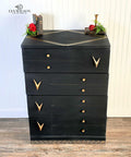 Dixie Belle Paint Midnight Sky Chalk Mineral Paint is the perfect paint for any DIY project! Black Chalk Mineral painted Mid Century dresser with gold accents and hardware. Staged with a red flower and book with candle stick.