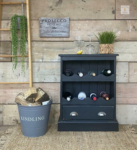 Dixie Belle Paint Midnight Sky Chalk Mineral Paint is the perfect paint for any DIY project! Black chalk painted wine cabinet with wine bottles inside and wine glasses, Also staged with a bucket of wood next to it.