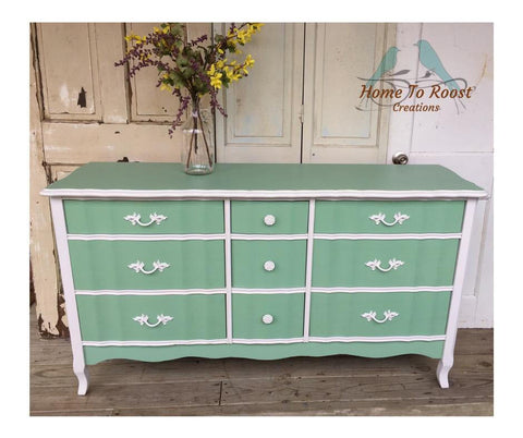 Dixie Belle Paint Mint Julep Chalk Mineral Paint is the perfect paint for any DIY project!
White chalk painted dresser with mint green chalk painted drawer fronts and top. Staged with a vase and yellow flowers.
