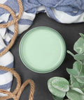 Dixie Belle Paint Mint Julep Chalk Mineral Paint is the perfect paint for any DIY project! Top view of Mint Julep Chalk Mineral Paint with a blue and white stripe towel, a rope and a plant staged around it.
