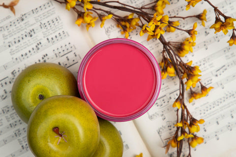 Dixie Belle Paint Peony Chalk Mineral Paint is the perfect paint for any DIY project! Top view of pink chalk paint can open staged next to apples, a plant and music sheets.