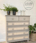 Dixie Belle Paint Putty Chalk Mineral Paint is the perfect paint for any DIY project! A muted taupe colored dresser featuring 2 short drawers next to each other on top with a basket weave stencil and 4 long skinny drawers underneath with a rattan like pattern surrounded by various potted greenery.