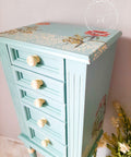 Dixie Belle Paint Sea Glass Chalk Mineral Paint is the perfect paint for any DIY project! A tall jewelry box painted in sea glass and wooden white hardware. There is a stencil in white on the top and a flower transfer on top of the jewelry box.