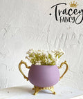 Purple chalk painted pitcher with gold legs and handles. Staged with white flowers inside, on a white painted distressed stool.