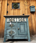 Dixie Belle Paint Stormy Seas Chalk Mineral Paint is the perfect paint for any DIY project!
Vanity cabinet painted in Stormy Seas Chalk Mineral Paint with a striped top drawer and silver hardware. Staged Infront of rustic wood door and wall with a wall mounted mailbox.