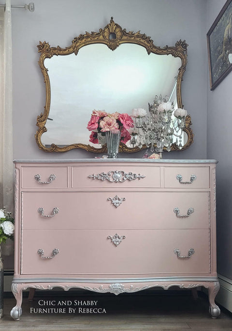 Dixie Belle Paint Tea Rose Chalk Mineral Paint is the perfect paint for any DIY project!
Beautiful elegant dresser given a makeover by painting it in Tea Rose Chalk Mineral Paint and using silver hardware with silver accent all around edge of the dresser. Staged with chandelier looking piece with flowers around and a clear glass vase.